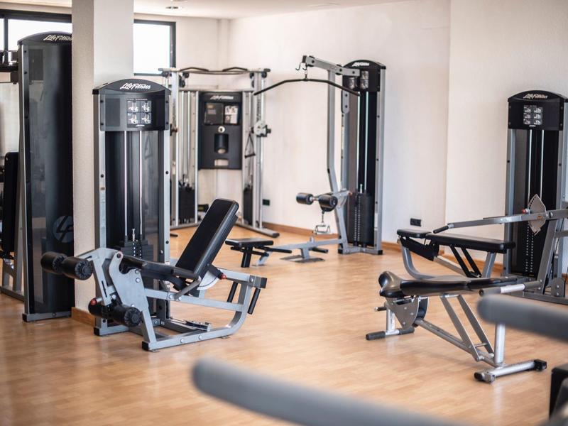 Moderne fitnessruimte met multifunctionele apparaten en houten vloer in lichte kamer.
