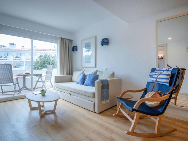 Lichte woonkamer met bank, fauteuil en groot raam met uitzicht op terras.