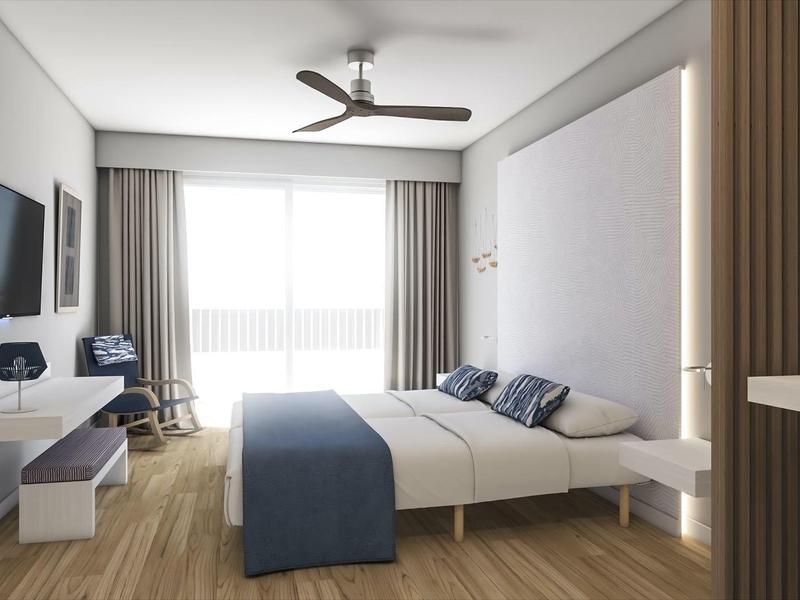 Modern hotelkamer met tweepersoonsbed, tv, ventilator en groot raam met gordijnen.