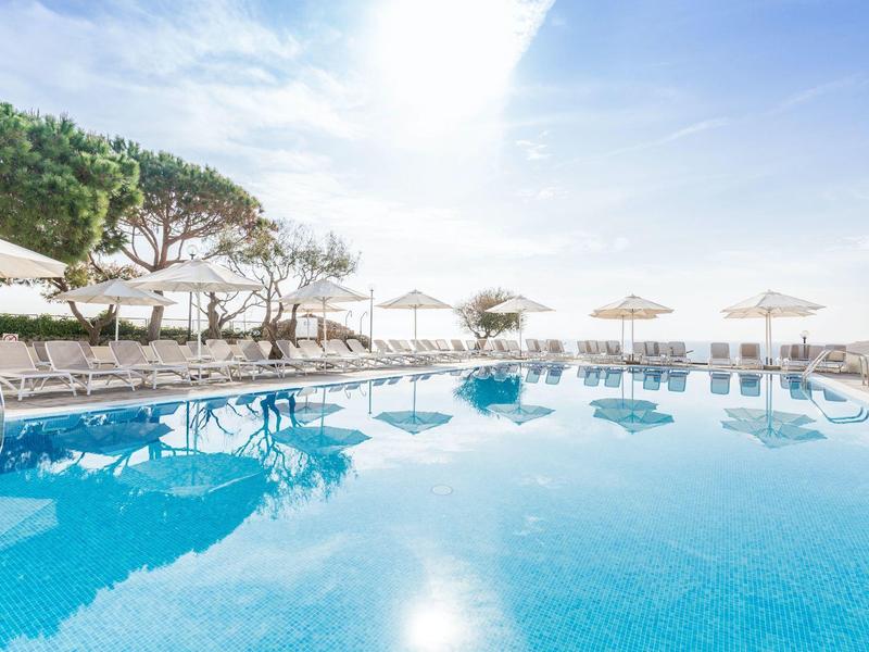 Groot buitenzwembad met witte parasols en ligbedden op een zonnige dag.