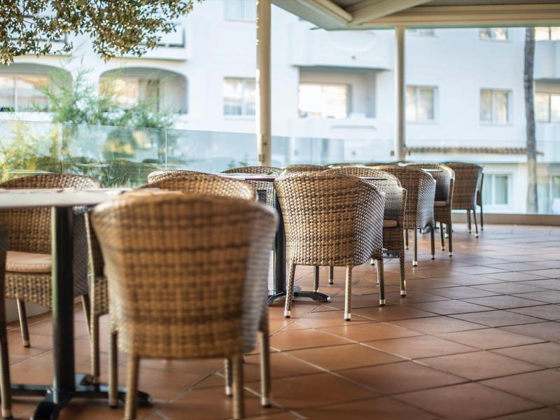 Buitenterras met meerdere rotan stoelen en tafels op betegelde vloer.