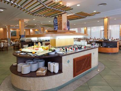 Strefa bufetu w jasnej restauracji hotelowej z różnymi potrawami i zastawą stołową.