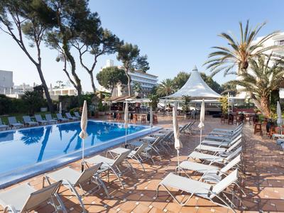 Strefa basenowa z leżakami, parasolami i śródziemnomorskimi drzewami w hotelowym ogrodzie.