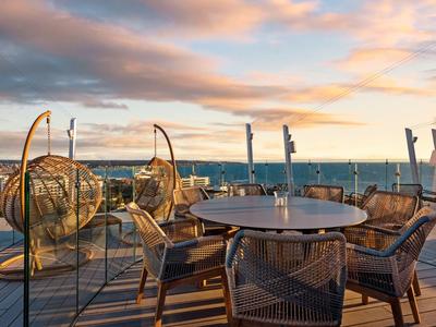 Terrazza con tavolo rotondo moderno, sedie e poltrone sospese con vista mare al tramonto.