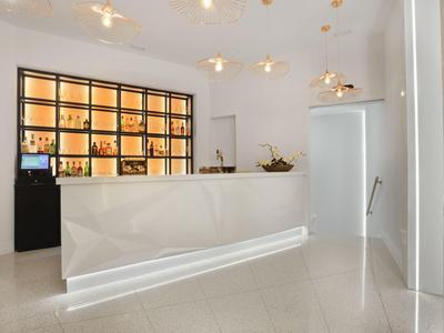 Reception moderna bianca dell'hotel con banco illuminato e scaffale a parete con bottiglie.