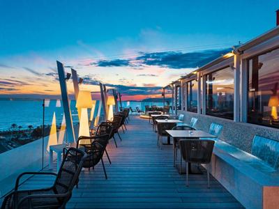 Nowoczesny taras hotelowy na zewnątrz z stołami, krzesłami i parasolami o zachodzie słońca.