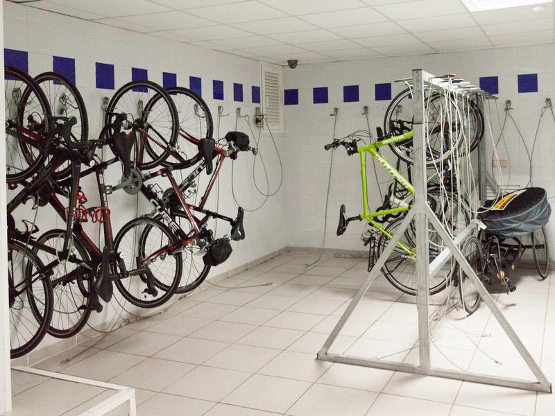 Pomieszczenie na rowery z kilkoma rowerami wiszącymi na ścianie i stojakiem pośrodku.