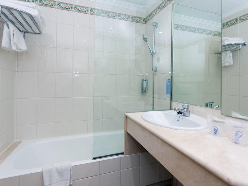 Jasna łazienka hotelowa z wanną, dużym lustrem i blatem z umywalką.