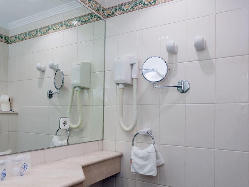 Łazienka wyłożona białymi kafelkami z dużymi lustrami, uchwytem na ręczniki i suszarką do włosów.