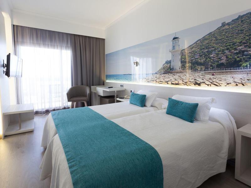 Nowoczesny pokój hotelowy z dużym łóżkiem podwójnym, turkusowymi akcentami i panoramicznym obrazem ściennym.