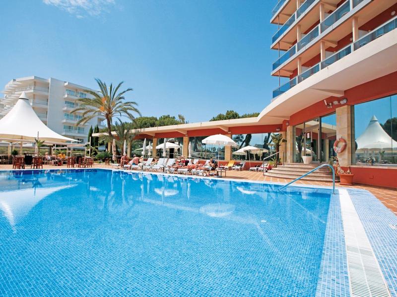 Duży basen hotelowy z parasolami, leżakami i palmami pod niebieskim niebem.