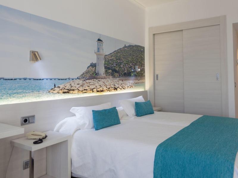 Nowoczesny pokój hotelowy z łóżkiem podwójnym, białymi ścianami i zdjęciem wybrzeża na ścianie.