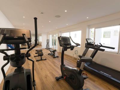 Moderner Fitnessraum mit Holzboden, Laufbändern, Fahrrädern und großen Fenstern für Tageslicht.
