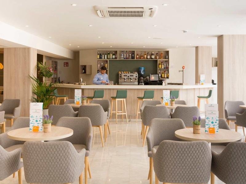 Bar d'hôtel moderne avec chaises confortables, tables rondes, éclairage clair et barman au comptoir.