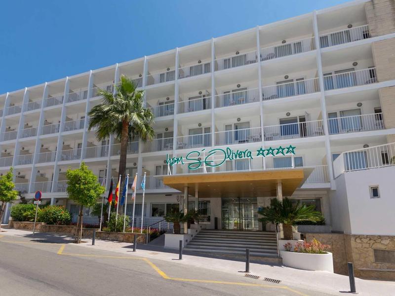 Hôtel moderne avec balcons, palmiers et ciel bleu clair.