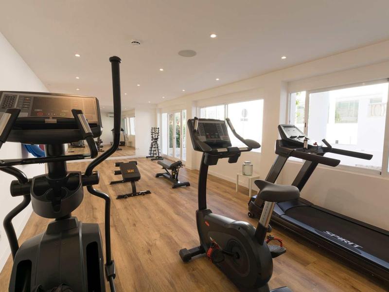 Salle de sport lumineuse avec appareils cardio, sol en bois et grandes fenêtres laissant entrer la lumière naturelle.