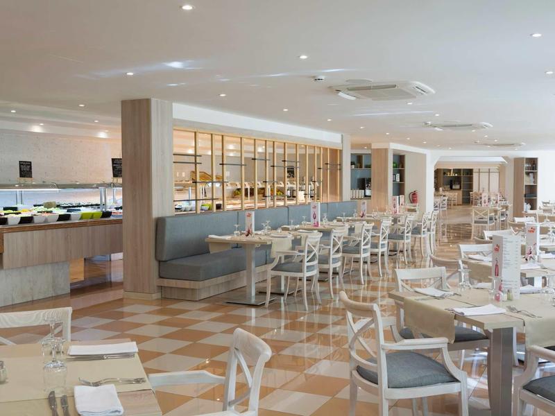 Salle à manger d'hôtel spacieuse avec tables en bois, chaises et buffets sous un éclairage encastré.