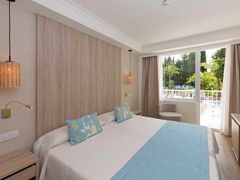 Chambre d'hôtel moderne avec lit double, accents bleus, balcon et lumière naturelle.