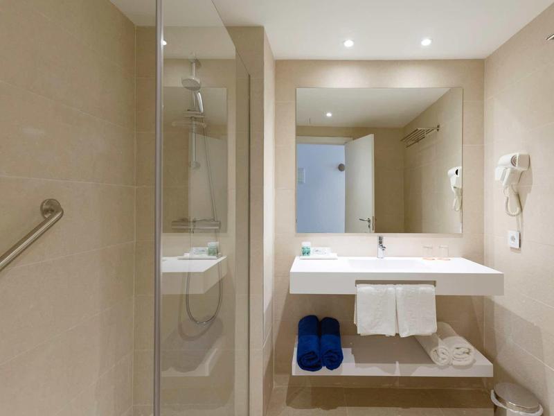 Salle de bain d'hôtel moderne avec douche, lavabo, serviettes et chaussons.