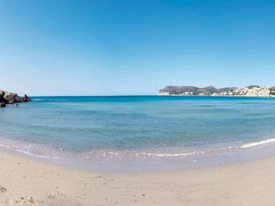 Szeroka piaszczysta plaża z przejrzystym, spokojnym morzem pod jasnym niebieskim niebem.