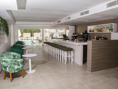 Area bar d'hotel moderna con poltrone verdi, bancone bianco e vista sulla terrazza soleggiata.