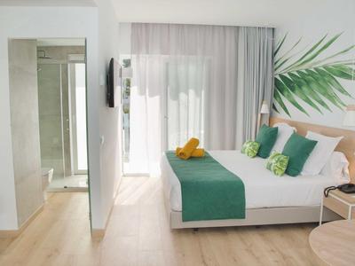 Jasny pokój hotelowy z podwójnym łóżkiem, zielono-białą dekoracją i dostępem do balkonu