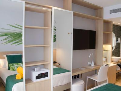 Nowoczesny pokój hotelowy z otwartą szafą, telewizorem i biurkiem z jasnego drewna.