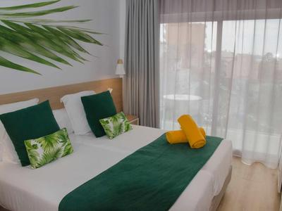 Nowoczesny pokój hotelowy z podwójnym łóżkiem, zielonymi akcentami i dużymi oknami z zasłonami.