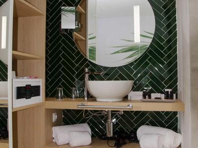 Nowoczesna łazienka z okrągłym lustrem, umywalką i zieloną ścianą z płytek.