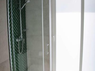 Nowoczesny prysznic z przeszklonymi drzwiami, zielonymi płytkami i matowym oknem w łazience.