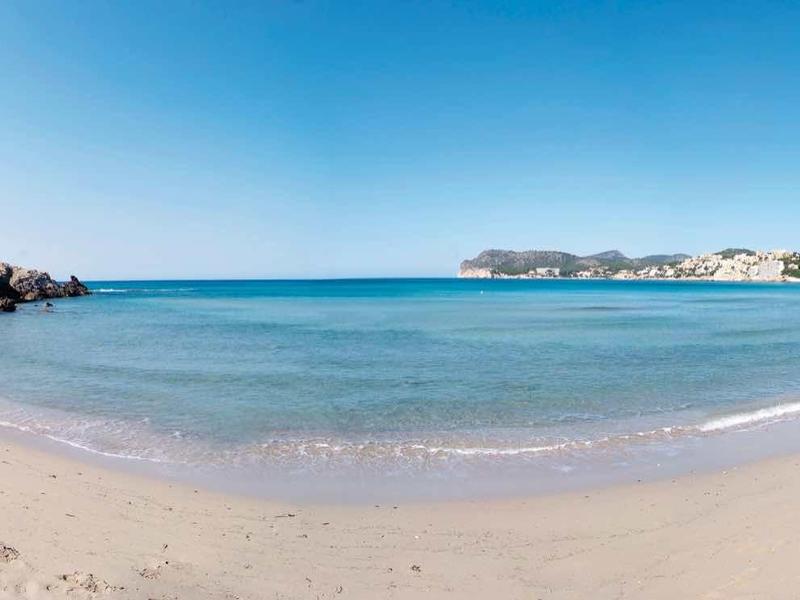 Szeroka piaszczysta plaża z przejrzystym, spokojnym morzem pod jasnym niebieskim niebem.