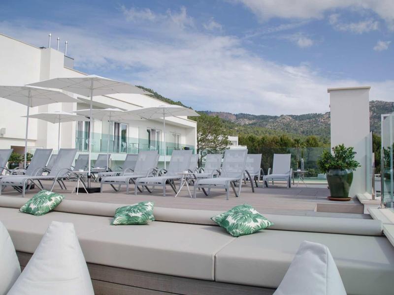 Nowoczesny taras na dachu z miejscem do wypoczynku i leżakami, szklane balustrady i góry w tle.