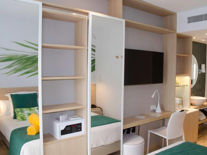 Nowoczesny pokój hotelowy z otwartą szafą, telewizorem i biurkiem z jasnego drewna.