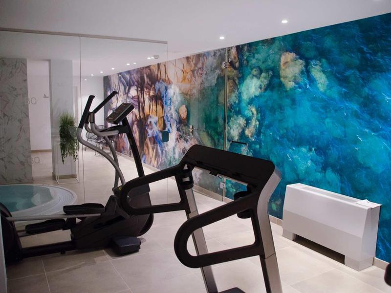 Nowoczesna siłownia z orbitrekiem i niebieską dekoracją ściany.