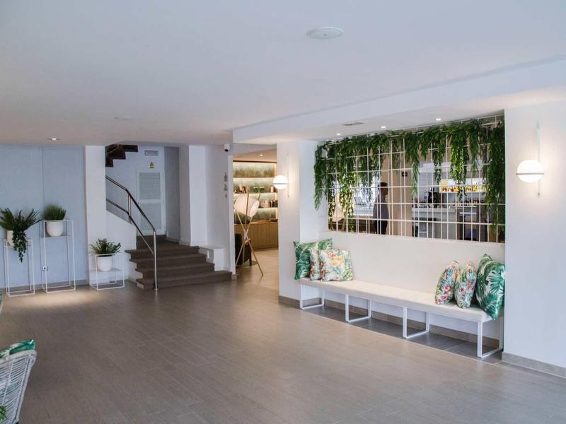 Jasne lobby hotelowe z ławką, roślinami i nowoczesną, czystą aranżacją.