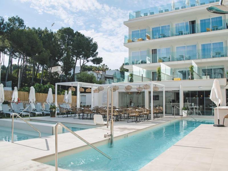 Nowoczesny basen hotelowy z leżakami i tarasem przed wielopiętrowym budynkiem w świetle dziennym