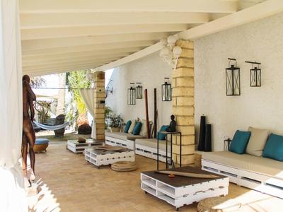 Terrazza soleggiata dell'hotel con comode sedute, cuscini e tavoli in legno sotto una veranda coperta.