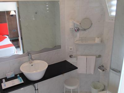 Bagno d'hotel moderno con lavabo bianco, grande specchio e letto rosso sullo sfondo.
