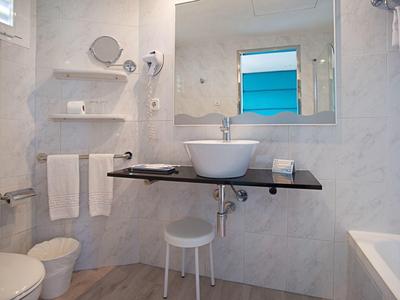 Bagno moderno con lavandino, specchio, sgabello e asciugamani in una stanza luminosa.