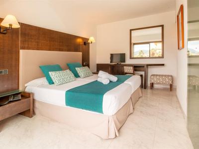 Camera d'hotel luminosa con grande letto matrimoniale, pareti in legno, TV e arredi moderni.