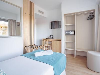 Camera d'hotel moderna con letto, armadio aperto, scrivania e grande specchio.