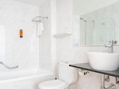 Bagno bianco minimalista con vasca, lavabo rotondo e grande specchio.