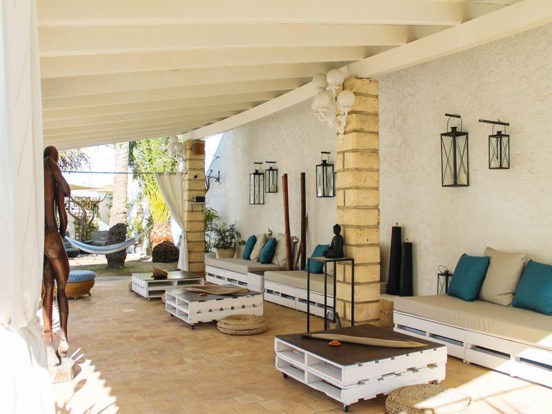 Terrazza soleggiata dell'hotel con comode sedute, cuscini e tavoli in legno sotto una veranda coperta.