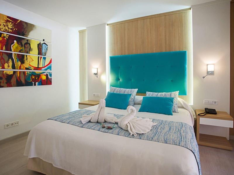 Camera d'hotel accogliente con letto matrimoniale, testiera turchese e arte murale colorata.