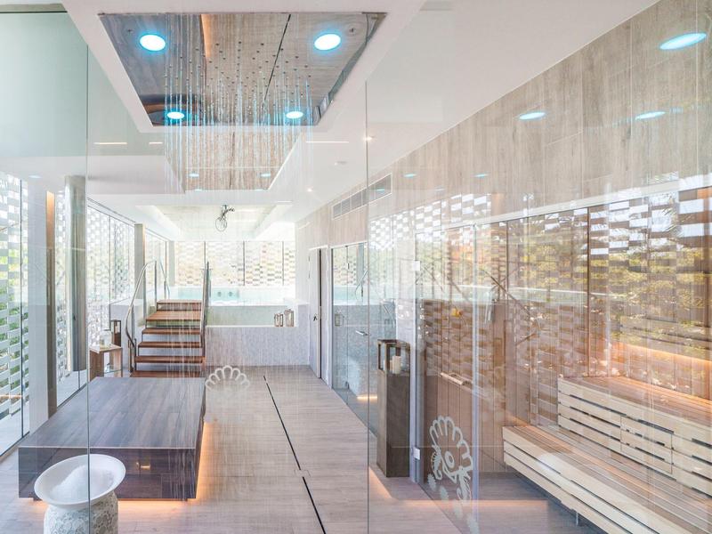 Area spa moderna con piscina riscaldata, sauna e pareti in vetro luminose.
