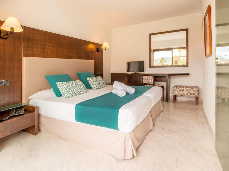 Camera d'hotel luminosa con grande letto matrimoniale, pareti in legno, TV e arredi moderni.