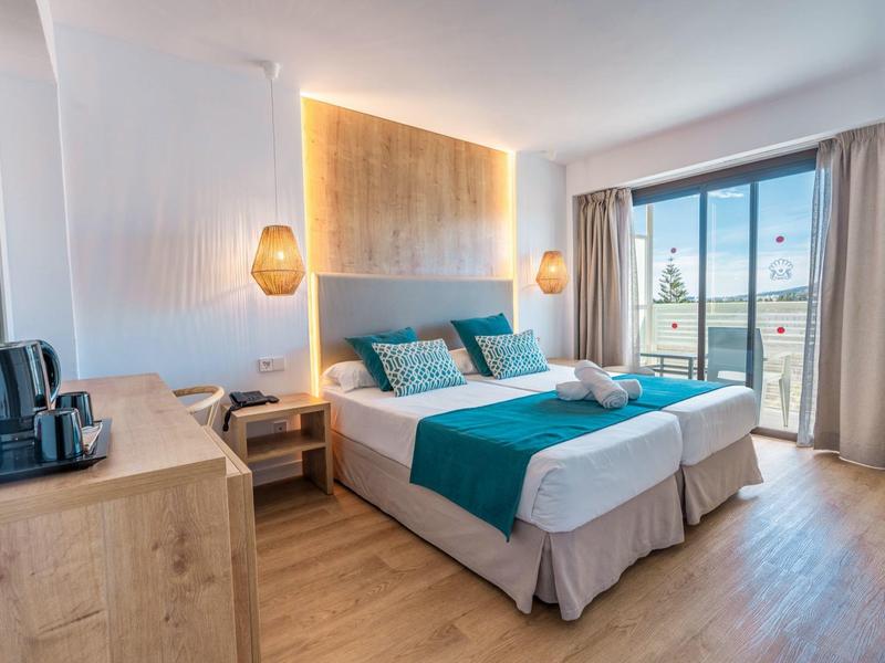 Camera d'hotel luminosa arredata con letto matrimoniale, mobili in legno e vista sulla città da grandi finestre.