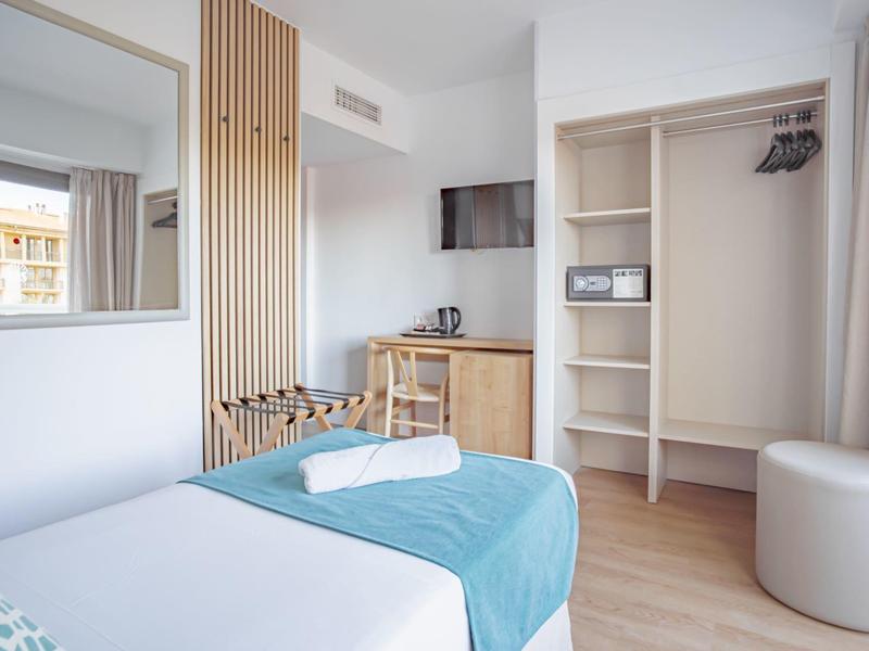 Camera d'hotel moderna con letto, armadio aperto, scrivania e grande specchio.