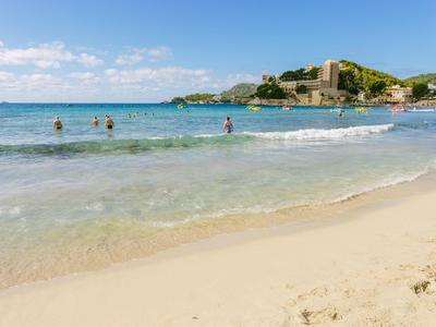 Beach with clear water, some swimmers, and a castle in the background under a blue sky
