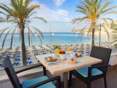 Terrasse avec vue sur la plage, la mer et les palmiers, table de petit-déjeuner dressée avec fruits et boissons.